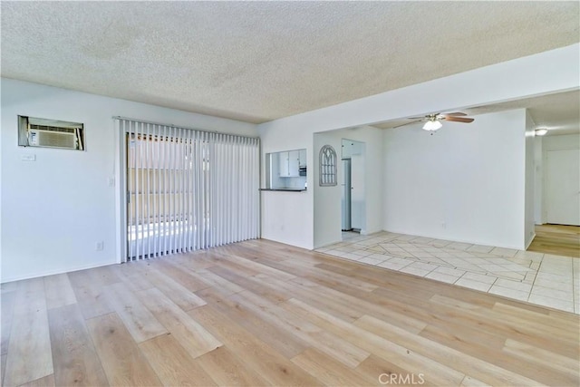 empty room featuring a wall mounted AC, ceiling fan, light hardwood / wood-style floors, and a textured ceiling