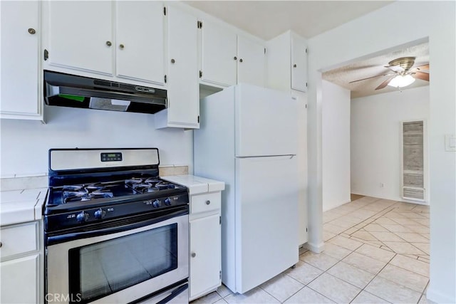 kitchen featuring stainless steel gas range oven, light tile patterned flooring, white cabinetry, and white refrigerator