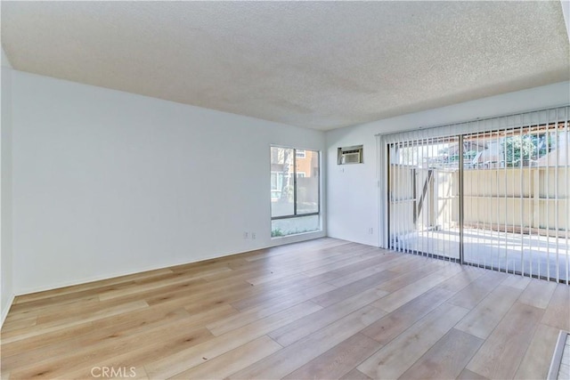 unfurnished room with light wood-type flooring, an AC wall unit, and a textured ceiling