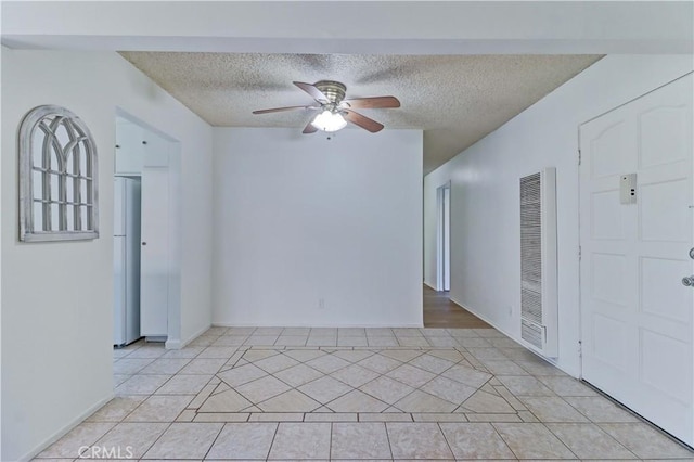 spare room featuring ceiling fan, light tile patterned flooring, and a textured ceiling