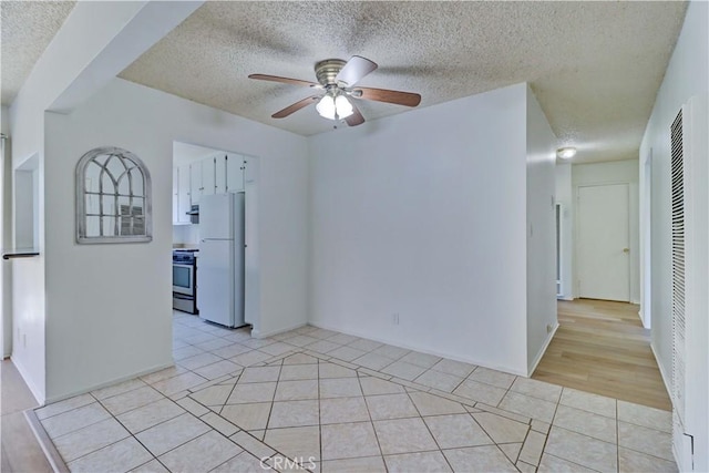 unfurnished room with ceiling fan, light tile patterned floors, and a textured ceiling