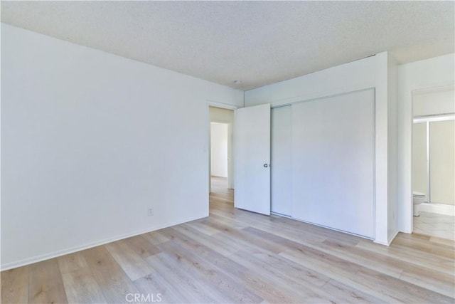 unfurnished bedroom featuring ensuite bath, a closet, light hardwood / wood-style floors, and a textured ceiling