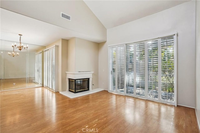 unfurnished living room featuring hardwood / wood-style floors, high vaulted ceiling, and an inviting chandelier