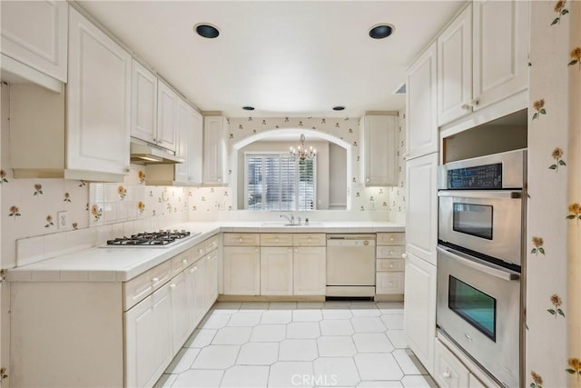 kitchen with white cabinetry, sink, an inviting chandelier, white appliances, and decorative backsplash