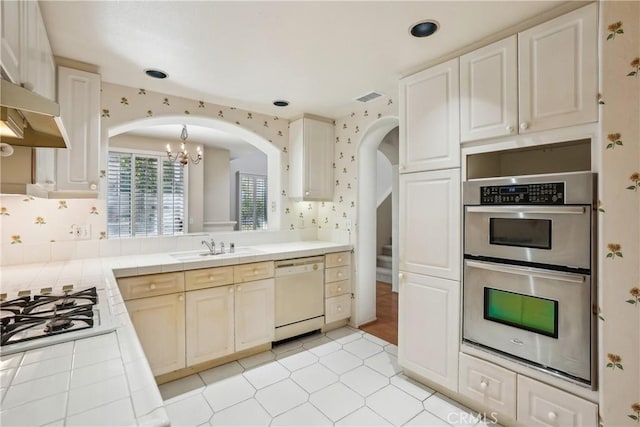 kitchen with sink, tile counters, range hood, a notable chandelier, and white appliances