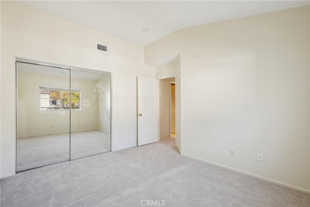 unfurnished bedroom featuring a closet, light colored carpet, and vaulted ceiling