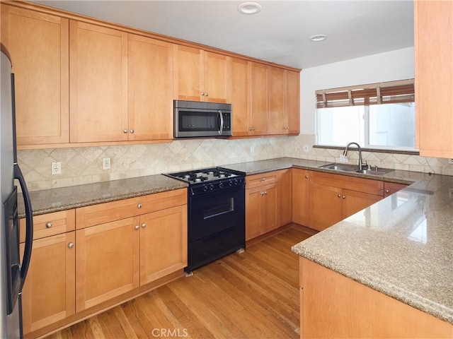 kitchen with appliances with stainless steel finishes, backsplash, light stone counters, sink, and light hardwood / wood-style flooring