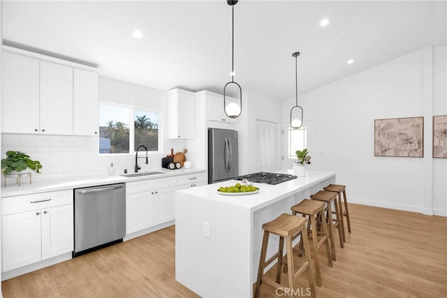 kitchen featuring decorative light fixtures, stainless steel appliances, a kitchen island, white cabinets, and sink