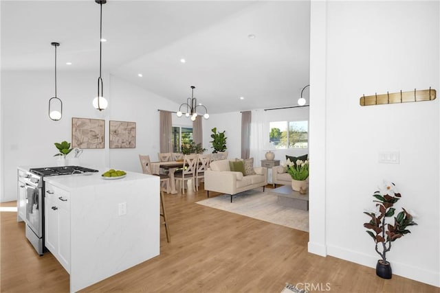 kitchen featuring white cabinets, a center island, light wood-type flooring, stainless steel gas range oven, and hanging light fixtures