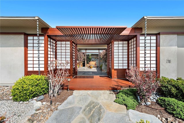 view of exterior entry with a pergola and a wooden deck