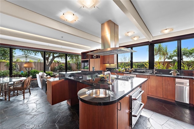 kitchen featuring island range hood, dark stone countertops, beamed ceiling, stainless steel gas stovetop, and an island with sink