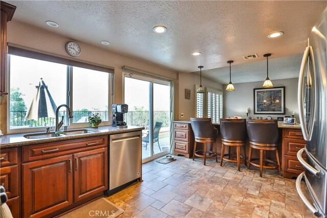 kitchen featuring appliances with stainless steel finishes, decorative light fixtures, a textured ceiling, and sink