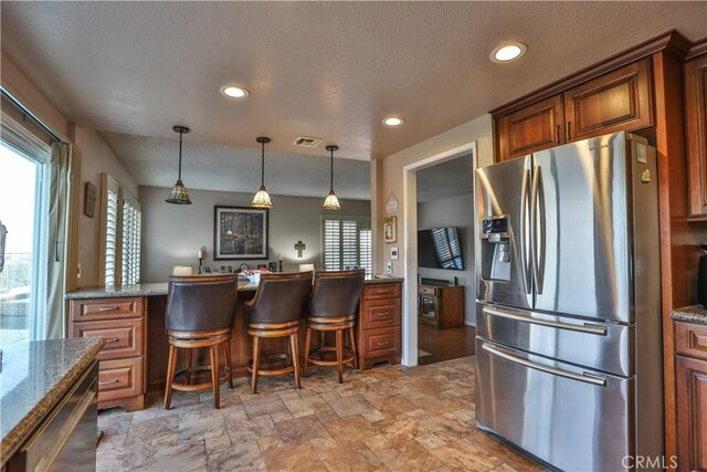 kitchen featuring a kitchen breakfast bar, pendant lighting, dark stone counters, and stainless steel fridge