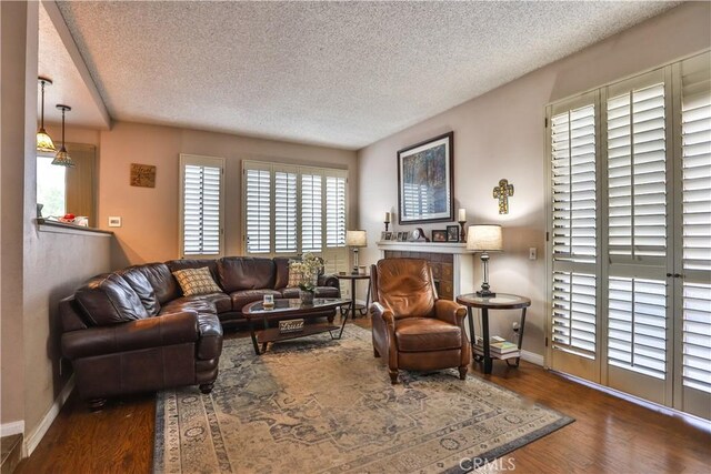 living room with dark wood-type flooring, a textured ceiling, and a tile fireplace