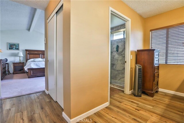 hallway featuring light wood-type flooring, a textured ceiling, and vaulted ceiling with beams