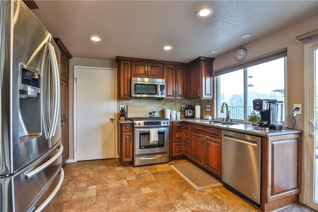 kitchen featuring sink, a textured ceiling, dark stone countertops, backsplash, and appliances with stainless steel finishes