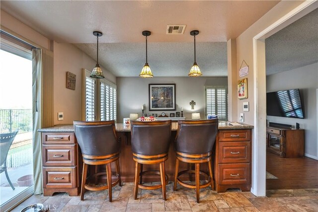 bar featuring a textured ceiling, a healthy amount of sunlight, pendant lighting, and light stone countertops