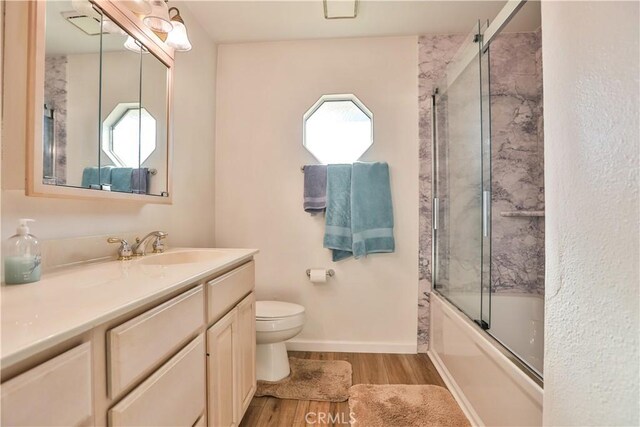 full bathroom with a wealth of natural light, bath / shower combo with glass door, toilet, and hardwood / wood-style flooring