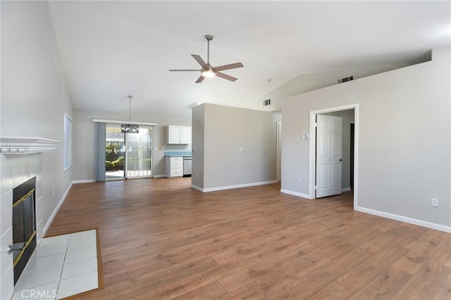 unfurnished living room featuring a tile fireplace, ceiling fan with notable chandelier, light hardwood / wood-style floors, and lofted ceiling