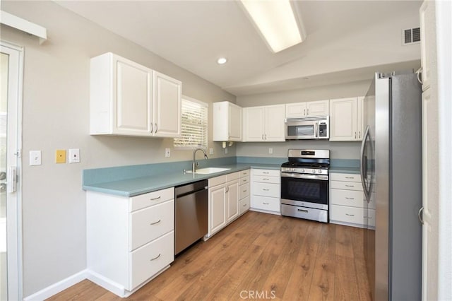 kitchen with lofted ceiling, white cabinets, sink, light hardwood / wood-style floors, and stainless steel appliances