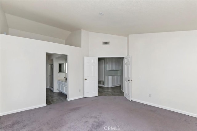 unfurnished bedroom featuring dark colored carpet, ensuite bathroom, and high vaulted ceiling