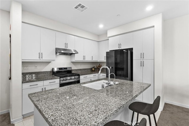 kitchen with black fridge with ice dispenser, sink, white cabinetry, stainless steel range with gas cooktop, and an island with sink