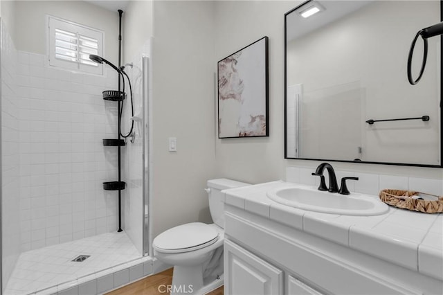 bathroom with hardwood / wood-style floors, toilet, vanity, and a tile shower