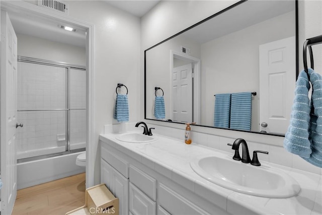 full bathroom with toilet, bath / shower combo with glass door, hardwood / wood-style flooring, and vanity