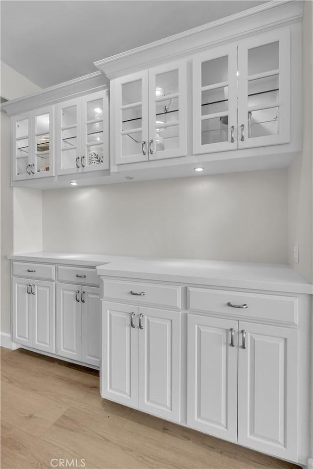 bar with light wood-type flooring and white cabinetry