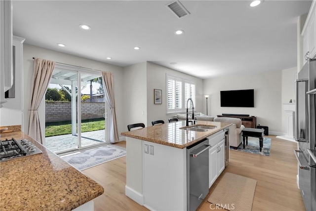 kitchen featuring white cabinetry, an island with sink, stainless steel appliances, light stone counters, and sink