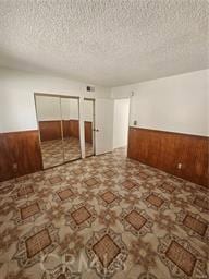 empty room featuring a textured ceiling and wood walls