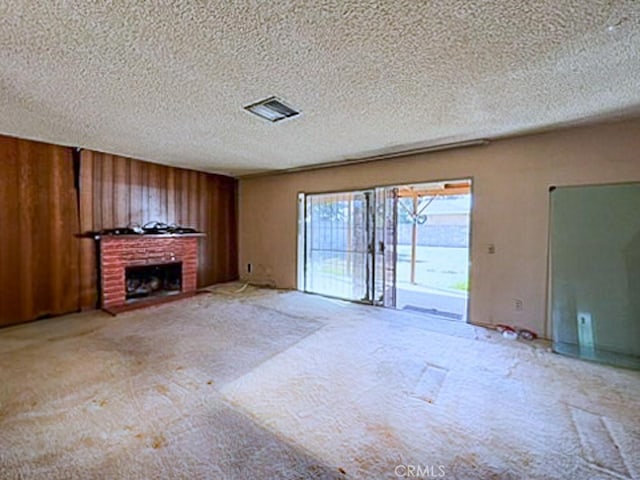 unfurnished living room with carpet floors, a textured ceiling, wood walls, and a fireplace