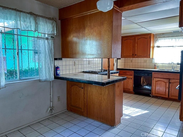 kitchen featuring kitchen peninsula, sink, black dishwasher, decorative backsplash, and tile counters