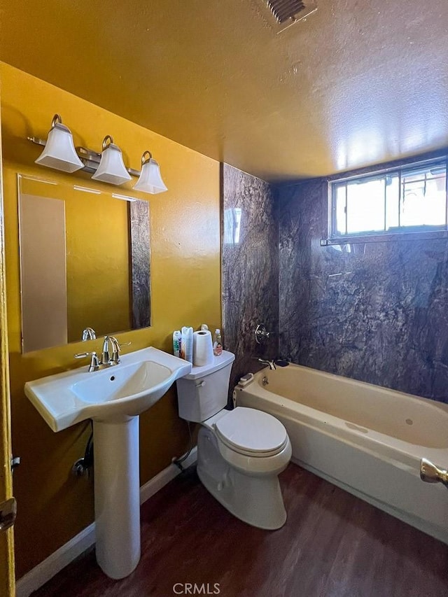 bathroom featuring a textured ceiling, hardwood / wood-style flooring, toilet, and tiled shower / bath combo