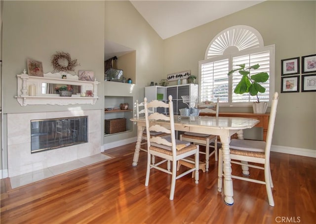 dining area featuring hardwood / wood-style flooring, a fireplace, and high vaulted ceiling