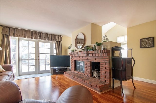 living room featuring lofted ceiling, a brick fireplace, wood-type flooring, and french doors