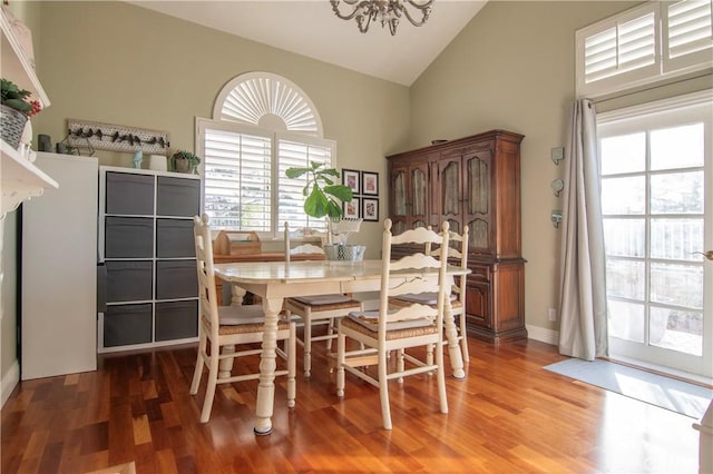 dining area featuring dark wood-type flooring, an inviting chandelier, and high vaulted ceiling