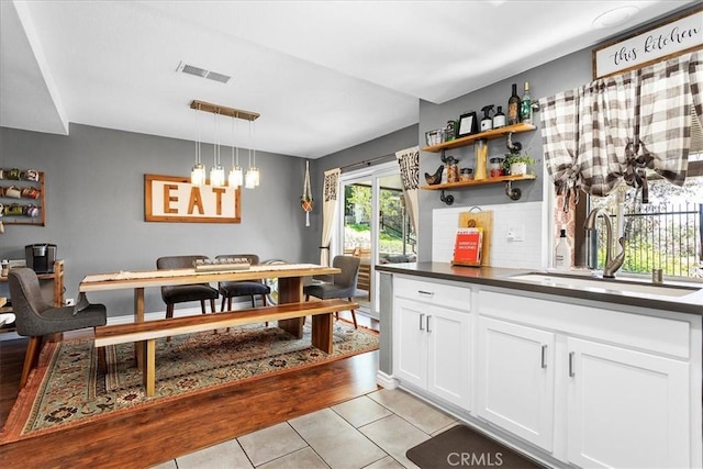 kitchen with white cabinets, sink, decorative backsplash, light tile patterned floors, and decorative light fixtures