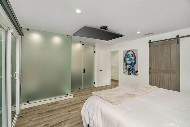 bedroom featuring a barn door, a baseboard heating unit, and hardwood / wood-style floors