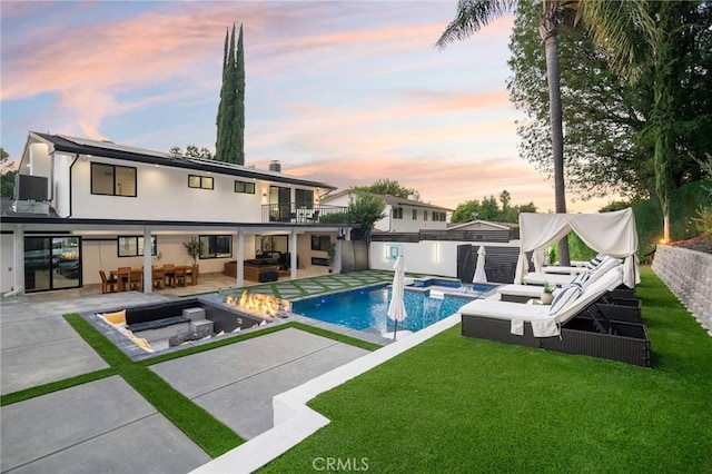 pool at dusk featuring an in ground hot tub, an outdoor living space with a fire pit, a yard, and a patio