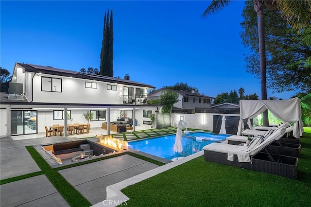 pool at dusk featuring a patio area, an in ground hot tub, a lawn, and an outdoor living space with a fire pit