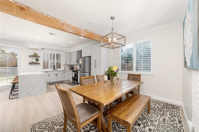 dining area featuring beam ceiling, sink, a notable chandelier, crown molding, and light wood-type flooring