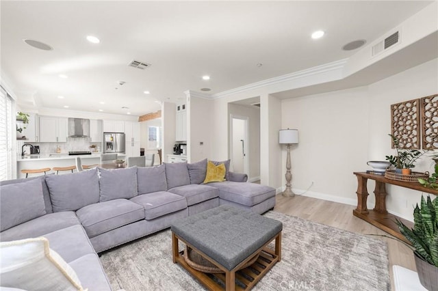 living room with light hardwood / wood-style floors, crown molding, and sink