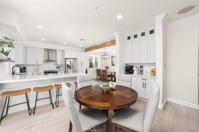 dining area with sink, beamed ceiling, light hardwood / wood-style flooring, and ornamental molding