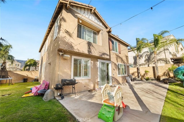 rear view of property featuring a yard, a patio, and a trampoline