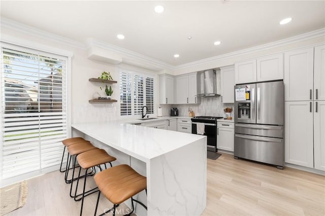 kitchen featuring kitchen peninsula, appliances with stainless steel finishes, sink, wall chimney range hood, and a breakfast bar area