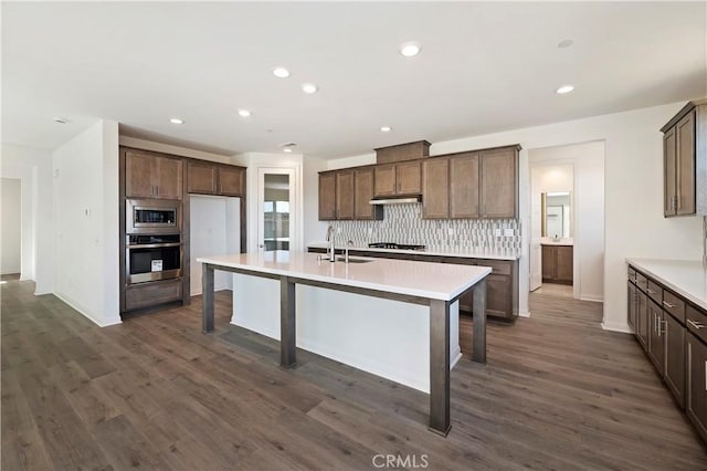 kitchen with sink, stainless steel appliances, dark hardwood / wood-style floors, an island with sink, and decorative backsplash