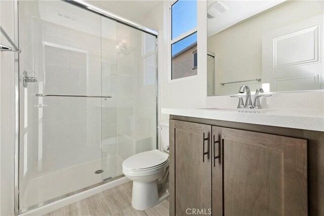 bathroom featuring hardwood / wood-style floors, vanity, a shower with shower door, and toilet