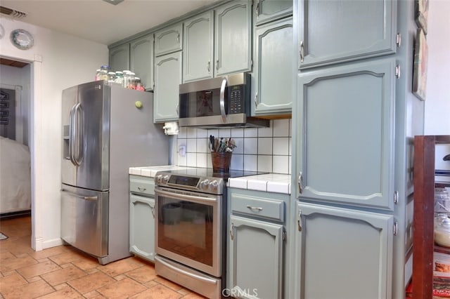 kitchen with tasteful backsplash, tile counters, and stainless steel appliances