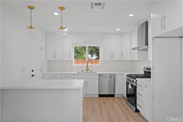 kitchen with sink, wall chimney exhaust hood, decorative light fixtures, white cabinetry, and stainless steel appliances